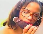 A girl wearing glasses sucking on a big black cock